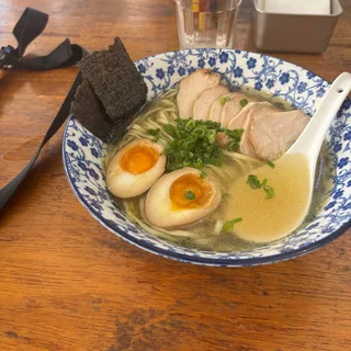 A bowl of ramen with chicken and eggs on a wooden table